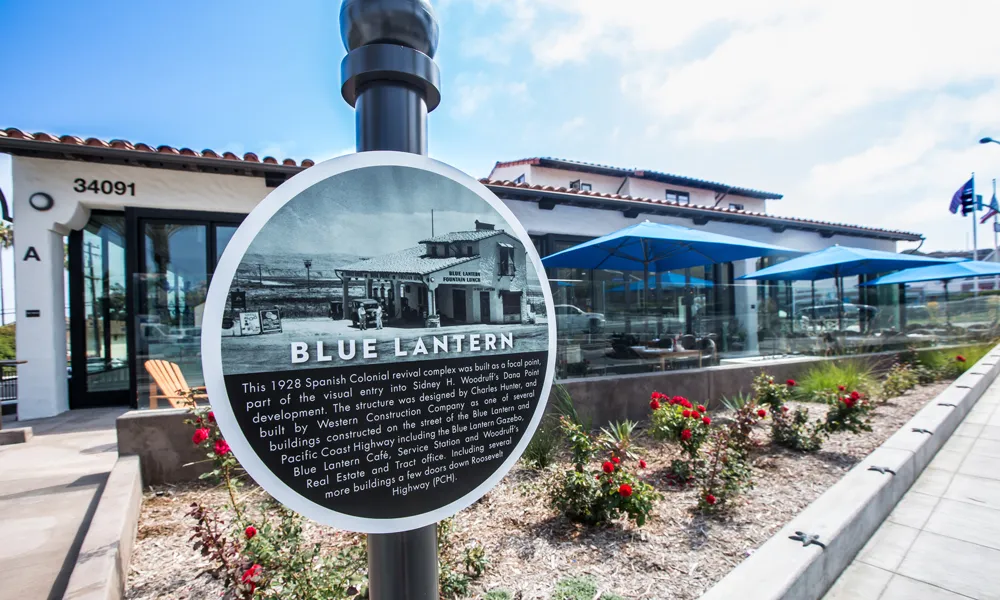 Round Blue Lantern historic marker in front of a white Spanish-style building