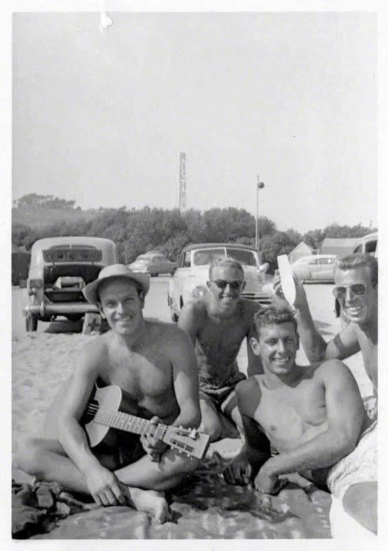 Men sitting on the beach beside parked cars, with the Richfield tower in the distance