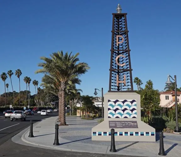 Tower-shaped PCH monument beside the highway, with palm trees behind