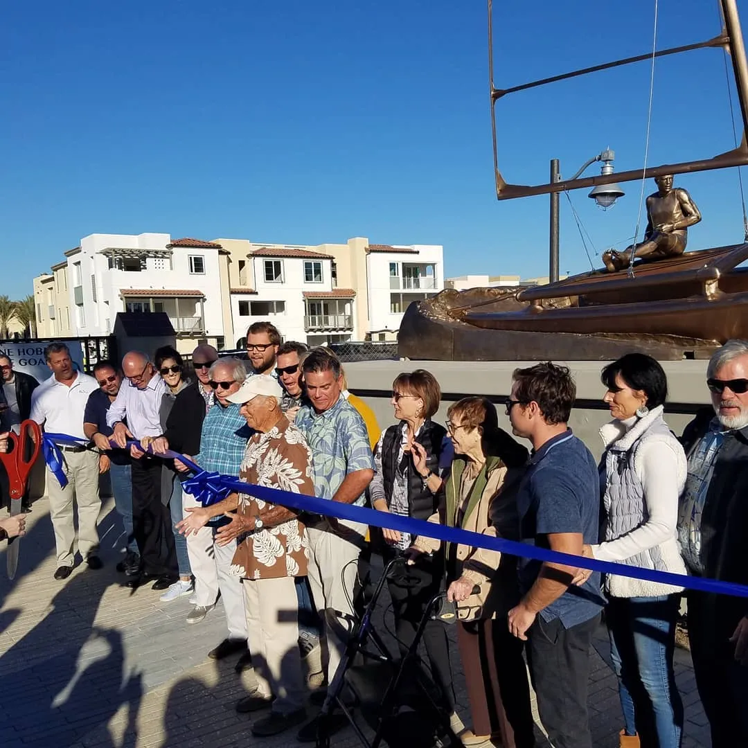 A crowd at a ribbon-cutting in front of a statue at Waterman’s Plaza